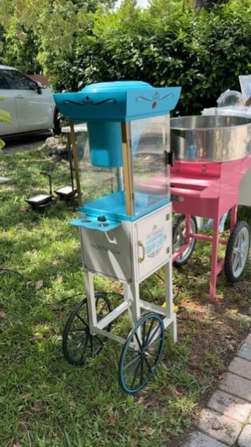 Outdoor event setup with a pink cotton candy machine and blue cart on a sunny day in Miami